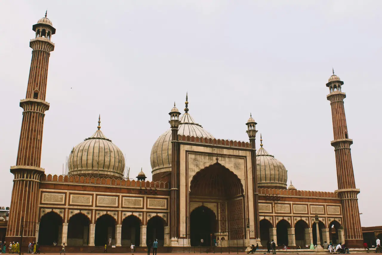 Front view of Jama Masjid in Delhi showcasing its grand domes, arched entrance, and tall minarets against a clear sky.