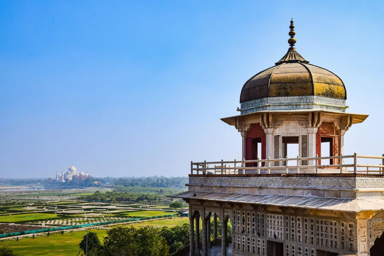 Scenic view from Agra Fort’s balcony pavilion overlooking the gardens and the distant Taj Mahal under a clear blue sky.