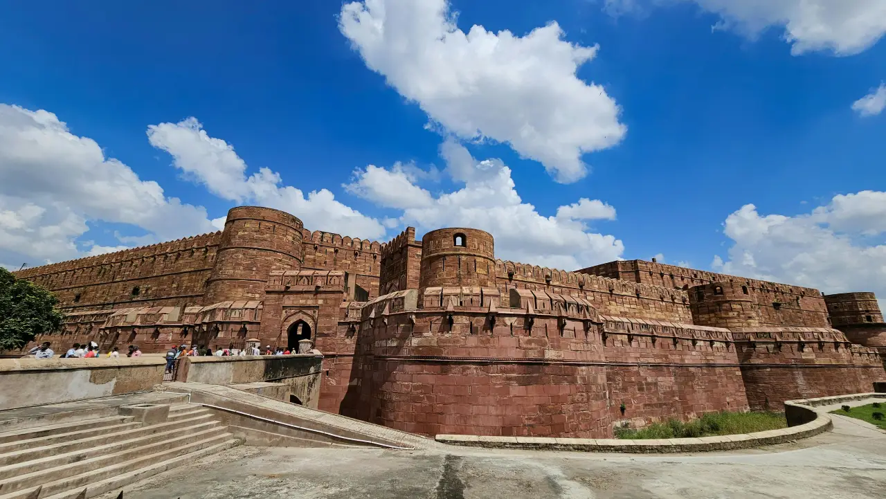 Panoramic view of Agra Fort with its massive red sandstone walls, arched gateways, and visitors exploring the historic Mughal fortress.