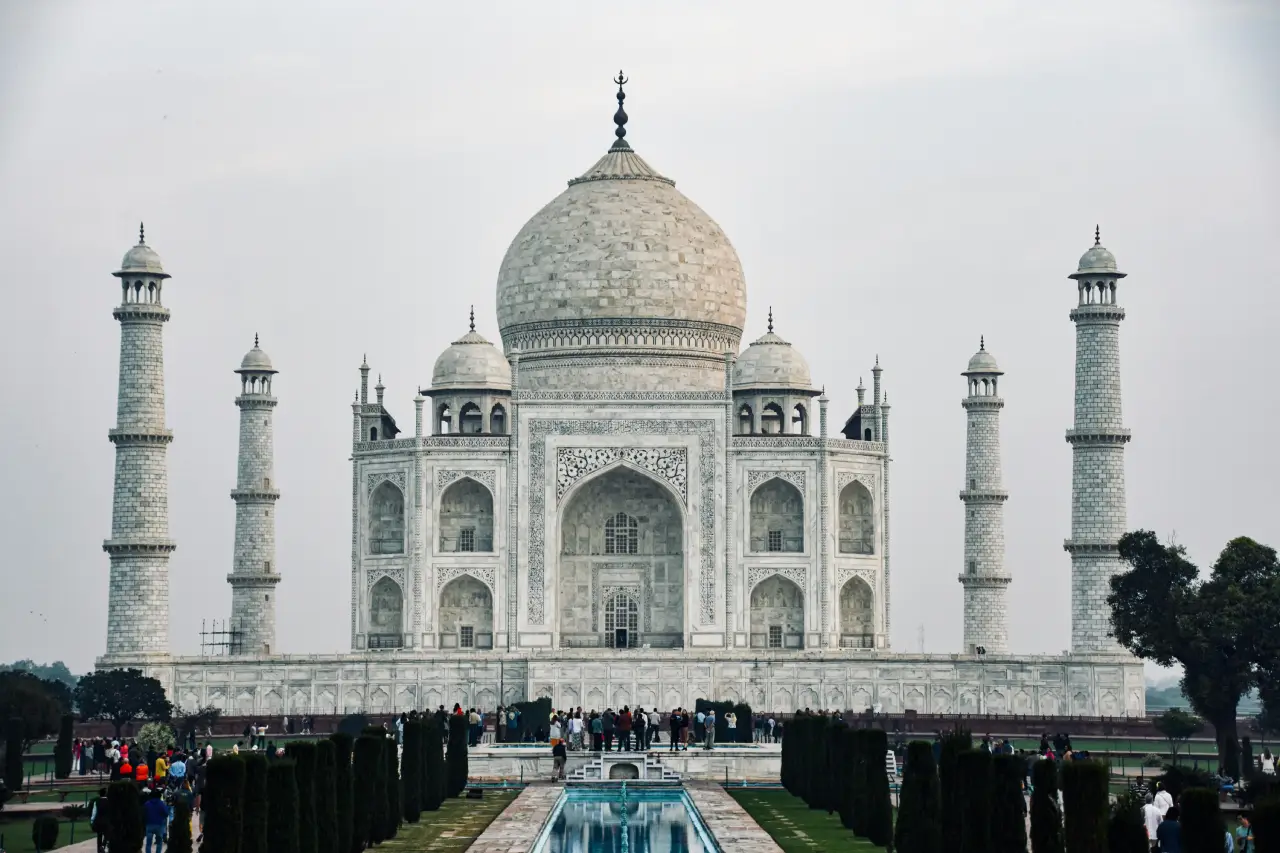 Front view of the Taj Mahal in Agra with its reflecting pool, minarets, and visitors exploring the monument.